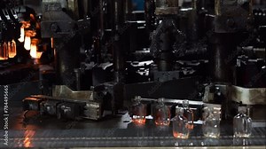 Complex machinery in an industrial plant producing transparent glass bottles, showcasing the manufacturing process and intricate equipment involved.