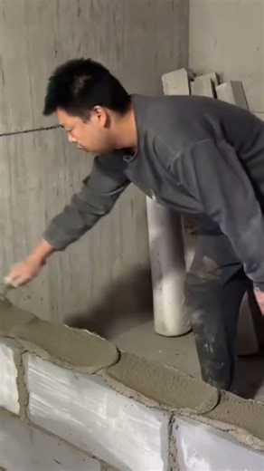 applying wet cement onto a concrete block wall with a trowel for precise bricklaying