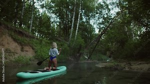 Young woman paddling on surfing board, standing on knees, man swimming after rowing on paddle board, back view. Female coach rows on surfboard. Sports lesson for beginners on water.