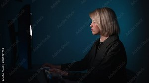 Blonde female writer typing computer keyboard late evening. Attractive young woman looking computer screen thinking on task in dark apartment. Professional businesswoman answering work email messaging
