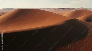 The wind gently shapes sand dunes under warm sunlight, revealing rippled textures in shades of orange and brown. Explore this arid desert landscape