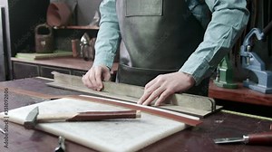 Working process of the leather belt in the leather workshop. Man holding crafting tool and working. Tanner in old tannery.