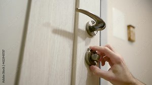 Male's hand screws on decorative glossy lids of a round shape for the lock cylinder in bronze color. Mounting a mortise door lock. The master installing lock in the door, final process. Close up video