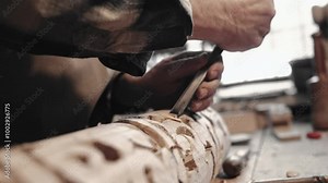 Caucasian male hands busy at work while using instrument for carpentry. With help of chisel creating crevices in long beam. Following lines drawn with pencil. Window with bright light in background.