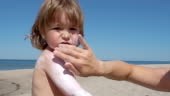 Mother applying sunscreen lotion on son back at beach. Mother...