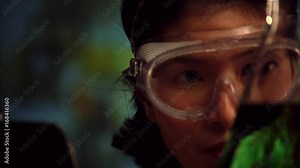 Female Asian scientist with goggles, beakers and clipboard.