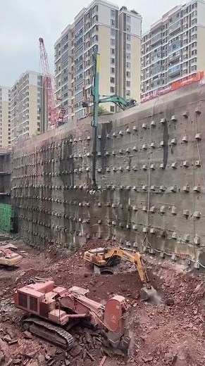 Anchored retaining wall shoring system reinforced with a telescopic grab bucket excavator.