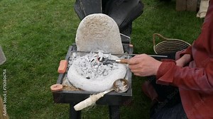 Viking blacksmith at work with a small, portable forge, focusing on metal craft against a natural backdrop. Perfect for showcasing historical craftsmanship and educational purposes