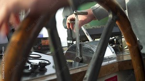 Captain turns steering wheel and controls throttle. Inside bridge of boat.
