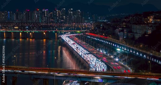High angle timelapse reveals flowing night traffic light trails across Gangbyeonbuk-ro expressway on Donho and Hannam bridges over Han River amid Seoul skyline and high-rise reflections