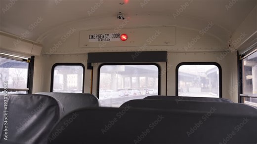 Interior view from the back of a school bus showing emergency door and windows during daytime. Public transportation vehicle cabin with empty seats.