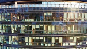 Offices in a modern high rise commercial building with glass facade. Sunset reflecting off the exterior of a corporate headquarters with suites for rent. Establishing aerial shot.