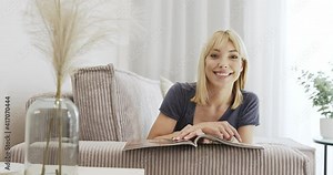 Reading the newspaper. Relaxing on the sofa, smiling woman reading a colorful magazine