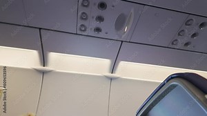 View of an aircraft cabin ceiling showing air vents, lighting controls, and speakers integrated into an overhead panel.