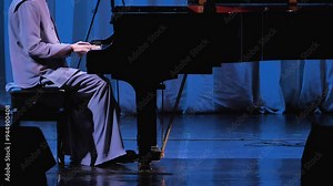A male pianist playing a grand piano on a stage in a concert hall. Black grand piano on a stage illuminated by blue light. Solo concert of classical music