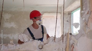 Contractor wrecks wall with sledgehammer making hole for rearrangement. Man doing manual dismantling and demolition works with big hammer hits for apartment renovation. Construction worker in uniform.