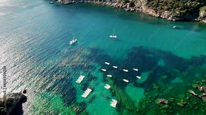 Aerial drone view to clear blue sea water with moored boats and yachts. Amazing azure nature background with coral reefs. Anchoring in bay in private beach on Corfu island, Greece travel destination.