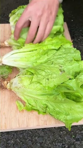 Hand prepares to cut fresh green lettuce on board