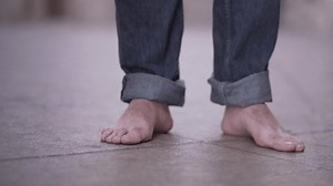Follow shot of barefoot man walking around the city wearing jeans