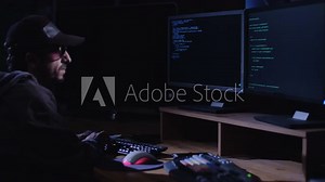 Cyber Terror - Computer Hacker sitting in a dark room in front of screens and writing lines of code while hacking