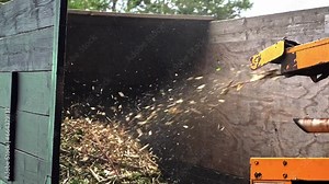 Wood chipper at work shredding tree branches and blowing them to truck in slow motion
