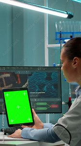 Vertical video: Microbiologist working on notepad with green chroma key display in modern equipped lab. Team of biotechnology scientists developing drugs using tablet with mock up screen.