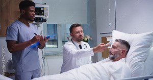 Handsome male professional doctor measuring temperature with infrared thermometer of Caucasian sick man patient in hospital while young African American nurse assistant writing down in medical history