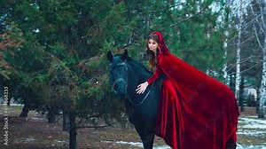 fantasy woman hand stroking neck back black horse. steed hair shines, Happy fairy tale princess Girl rider riding a horse smiling face, red vintage long dress cloak cape head hood. Forest green trees