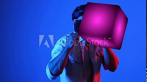 Skilled gamer boxing and punching floating box while wearing VR glasses to connect metaverse. Male model using virtual reality goggles while exercising and standing at neon background. Apparatus.
