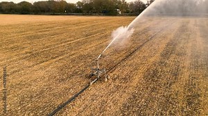 High angle aerial shot of field irrigation system watering crops. Arc of water seen from up close. Drone footage of farm spray head shooting water a long distance.