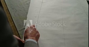 A tailor drawing and cutting a cloth according to the tradition of tailors.