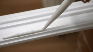 Process of applying glue on white baseboard surface with industrial tube, white sealant for plinth installing on construction site, using adhesive materials for home improvements. High quality 4k