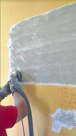 Using a drywall sander with vacuum to smooth a wall before painting