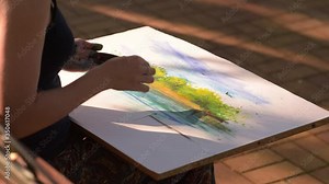 A girl paints a picture with her fingertips in a Park among trees and green bushes