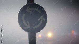Blue arrow roundabout sign with traffic vehicle drive at fog night at background. Low visibility from air pollution