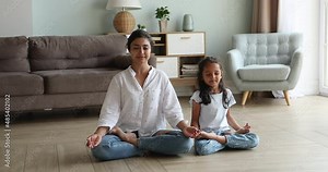 Attractive Indian yogini mom teach good life habits her cute little 6s daughter, sit on warm floor cross-legged, do meditation practice together in living room. Yoga at home, healthy lifestyle concept