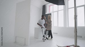 Behind the scenes of a photo shoot: A beautiful black model football player is preparing for a photo shoot for a magazine, a makeup artist corrects the tone of the skin for photos in a sports magazine