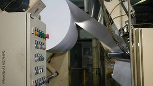 Manufacturing, recycling, industry and automated technology equipment. Part of automatic plastic making machine - moving roller with white paper. Plastic film roll unreeling for furniture production