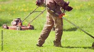 Professional gardener mowing lawn at central park property with gasoline brush cutter. Sunny day