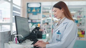Una farmacéutica profesional que utiliza una computadora para investigar medicamentos y volver a comprobar las existencias de productos en la farmacia.