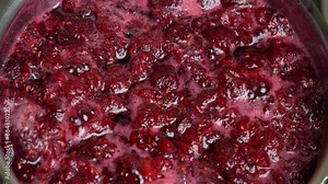 Preparation of freshly picked red raspberries with sugar to make raspberry jam, close up. Cooking homemade raspberry fruit jam in a saucepan. Boiling raspberry fruits for jam