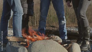 Outdoor, a group of people standing around a fire. People in nature are warming themselves around a fire.