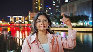 4K Portrait of confident Indian woman vlogging at Clarke Quay during night at Singapore city. Stylish female tourist filming a video and introducing tourist attractions. Holidays and travel concept.