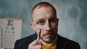 Man detective, attractive bearded man is looking in camera with magnifier. Young scientist uses magnifying glass to zoom and peer the object in laboratory, investigation process. Solving the crime