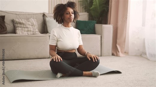Daily morning workout, black woman sitting in lotus position and warming neck. Beautiful african american lady doing sport and practicing yoga for stay healthy and slender in middle age, training
