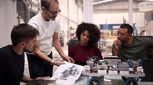 Multi generation and multiracial team of engineers examining a blueprint and working on a robotics project in a factory