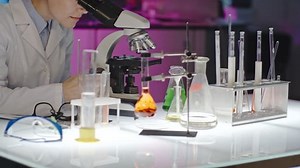 Curly female scientist in glasses looking into microscope in laboratory, then looking up and posing for camera
