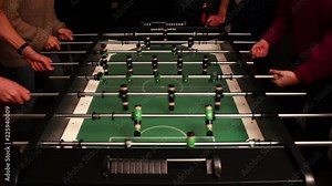Four people playing table football / table soccer / foosball. The football table and their hands are shown from above.