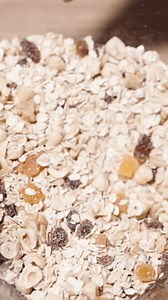 Vertical video. Ingredients for Granola, grains and a mixture of nuts and fruits, are being mixed together in a large bowl.