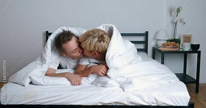 Young gay couple lying on bed together in bedroom, hugging and kissing. LGBT family